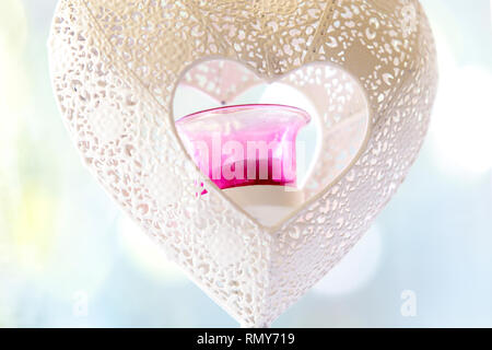 Chiudere l immagine di un cuore bianco a forma di ferro portacandele con vetro rosa tea isolato di luce con una bella luce blu bokeh di fondo. Concetto per amore. Foto Stock