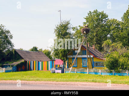 Cicogne a sedersi in un nido su un lampione vicino a casa colorati con un bene . La Bielorussia, Polesie. Foto Stock