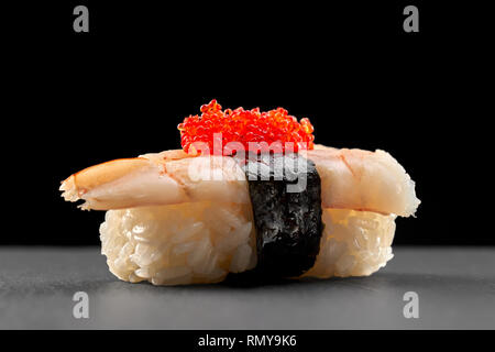 Ebi nigiri sushi in pietra nera piastra. Riso con gamberetti, avvolto in nastro di Nori e guarnita con red flying fish roe. Foto Stock