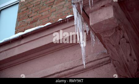 Inverno ghiaccioli fusione su tetto sotto il sole di primavera e gocciolamento dai loro suggerimenti Foto Stock