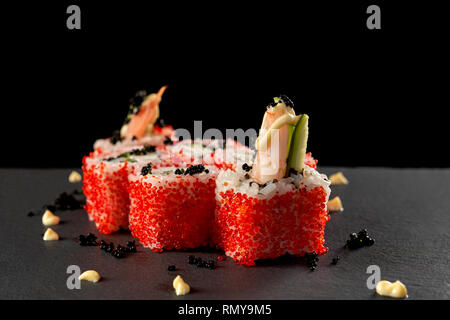 Giapponese uramaki rotoli di riso con gamberetti, cetriolo, coperto con red flying fish roe. Vulcano sushi decorate con la salsa e caviale nero. Foto Stock