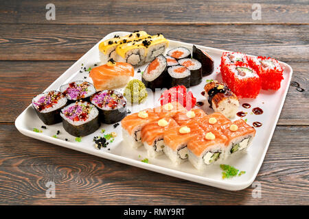 Gustosi piatti Sushi set di rulli di Philadelphia, vegetariane maki, sake maki, sake nigiri, unagi nigiri e panini al formaggio. Sushi servita con mayo, salsa, wasabi e zenzero sott'aceto, sulla piastra bianca. Foto Stock