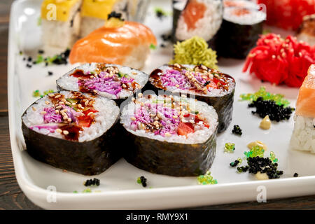 Maki Vegaterian close up, sulla piastra bianca con altri tipi di sushi. Veggie panini con verdure, cavolo viola, cetriolo, servita con sause, decapati zenzero e wasabi. Foto Stock