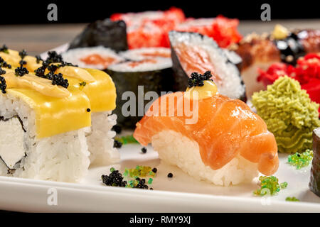 Bene il nigiri e panini al formaggio vicino. Una gustosa cucina giapponese. Set di uramaki e maki sushi decorate con mayo, caviale nero, serviti con wasabi sulla piastra bianca. Foto Stock