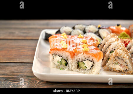 Close up di deliziosi panini di Philadelphia, coperto con salmone e decorate con mayo. Sushi set di diversi tipi di uramaki e rotoli maki, triangolo uramaki servita su piastra bianca. Foto Stock