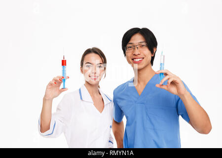 Certi giovani medici multietnica giovane indossano uniformi isolato permanente su sfondo bianco, mostrando le siringhe Foto Stock