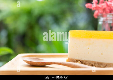 Frutti della passione cheesecake servire su legno tay e tavolo in legno con secchi vaso portafiori verde sullo sfondo della natura Foto Stock