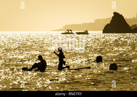 Immagine di una silhouette di una giovane coppia pagaiando su un surf al tramonto in Maro, Andalusia, Spagna. Foto Stock