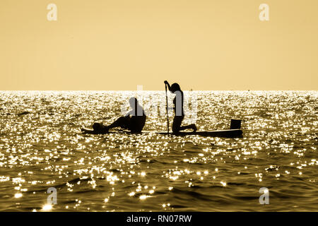 Immagine di una silhouette di una giovane coppia pagaiando su un surf al tramonto in Maro, Andalusia, Spagna. Foto Stock