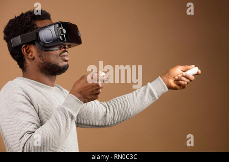 Di carnagione scura millenario il turista in un abbigliamento informale con gli occhiali con testa-display montato per smart phone, operando con i controller in mani, il DOI Foto Stock