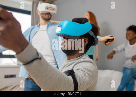 Gruppo di multirazziale maschio femmina amd gli studenti la riproduzione di gioco virtuale utilizzando occhiali VR, divertirsi insieme ay home - Virtual omg la realtà e portatile di Foto Stock