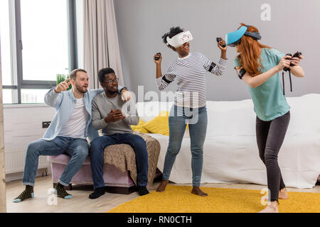 Gruppo di giovani multiculturale di diversi amici utilizzando la realtà virtuale auricolari divertendosi al campus universitario. Ragazza africana e caucasico i capelli rossi donna Foto Stock