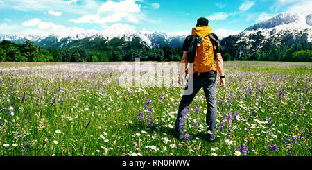 Escursionista con zaino in un prato di fiori godendo la vista sulle montagne Foto Stock
