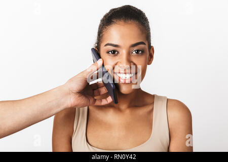 Felice giovane donna africana seduto mentre la mano d'uomo tenendo il telefono cellulare al suo orecchio isolate su sfondo bianco Foto Stock