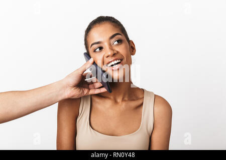 Felice giovane donna africana seduto mentre la mano d'uomo tenendo il telefono cellulare al suo orecchio isolate su sfondo bianco Foto Stock