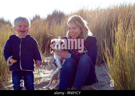 Una madre e figlio sorridente giocando con il cane in erba lunga Foto Stock