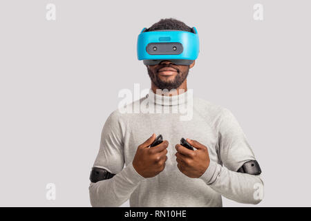 Maschio africano gamer sperimentando gioco di boxe con gli occhiali VR, copricapo e simulazione 3D attraverso la realtà virtuale bicchieri isolate su uno sfondo grigio. Foto Stock