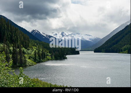 Vista sul lago Duffey, con coperto il cielo sopra la montagne coperte di neve, circondata da una foresta, lungo l'autostrada 99, vicino a Whistler, British Columbia, Canada Foto Stock