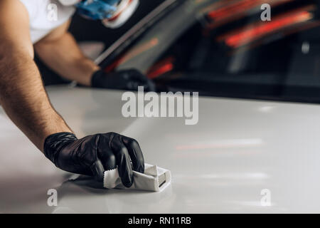 Giovanissimo meccanico in maschera attentamente il lavoro presso il garage. close up foto ritagliata. La messa a fuoco su un guanto nero con un panno Foto Stock