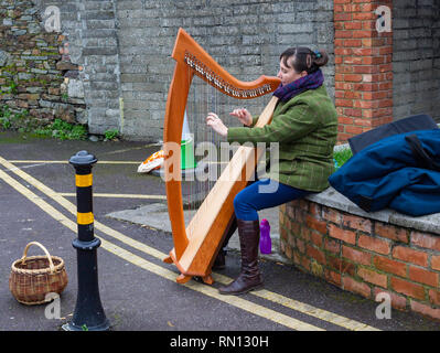 busker femminile che gioca un'arpa per soldi seduti su un muro di mattoni Foto Stock