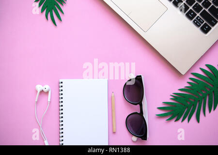 Spazio di lavoro in una rosa di colori alla moda o di design d'estate con un concetto per iniziare una vacanza. Laptop e varie cose nelle vicinanze. Foto Stock