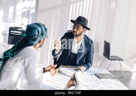 Due razza mista fiducioso focalizzato esperti maschio analizzando il risultato aziendale seduta a tavola in Cliente ufficio moderno in Medio Oriente Foto Stock