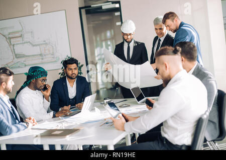 Interracial gruppo maschile di architetti e costruttori sono impegnati in un vivace dibattito di bilancio e di piano di costruzione per un nuovo oggetto. Foto Stock