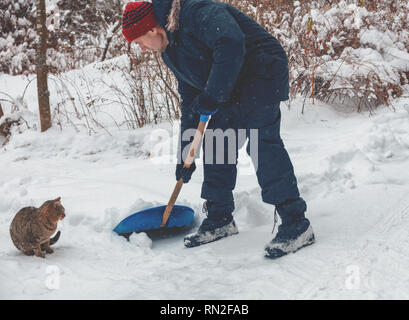 Un uomo con la pala pulisce la strada dalla neve nella neve. Cat si trova nelle vicinanze Foto Stock