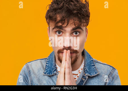 Close up di un giovane uomo barbuto casualmente vestito per chiedere qualcosa di isolato su Orange Foto Stock