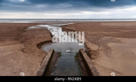 Un piccolo fiume che taglia un canale attraverso la spiaggia sabbiosa a Saltcoats e Ardrossan sulla via di Clyde beach in Ayrshire. Foto Stock