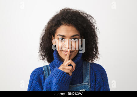 Primo piano di una bella giovane donna africana che indossa un maglione in piedi isolato su sfondo bianco e mostra il gesto di silenzio Foto Stock