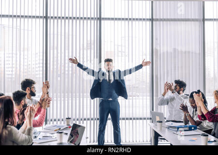 Business, successo, gesto e concetto di persone - Retro di giubilanti imprenditore i bracci di sollevamento e celebrare il trionfo sulla panoramica nella finestra di office e Foto Stock