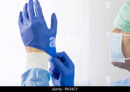 Medico chirurgo in guanti sterili preparando per il funzionamento in ospedale. Indossa il cappuccio chirurgico e abito blu Foto Stock