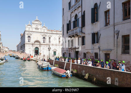 Gruppo di tour a piedi attraverso il Castello, Venezia, Italia su un canale nella parte anteriore del Campo dei Santi Giovanni e Paolo e la Scuola Grande di San Marco Foto Stock