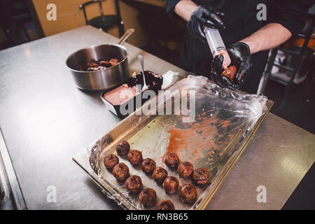 Cucina a tema. Le mani vicino. giovane uomo caucasico in nero uniforme e guanti in lattice in cucina. ristorante prepara la carne macinata di manzo e conduce in berry Foto Stock