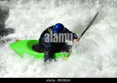 Kayaker è circondato da acqua bianca sulle rive di un fiume in Tennessee. Il kayak è di colore verde e casco è blu. Foto Stock