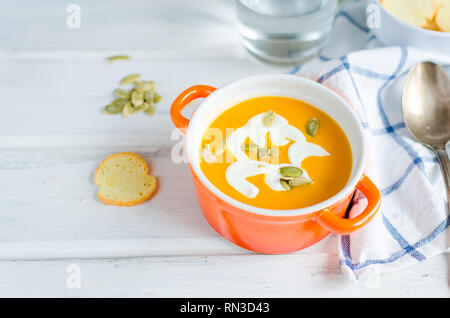 In casa la zuppa di zucca in vaso di ceramica con semi e panna acida e crostini di pane bianco rustico sfondo di legno Foto Stock