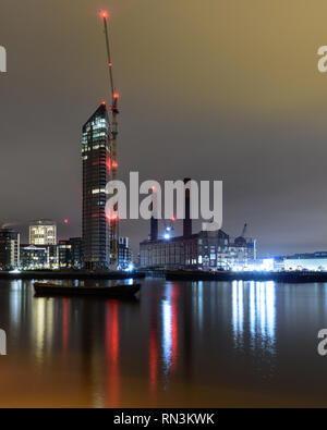 London, England, Regno Unito - 28 dicembre 2018: gru a torre sono illuminate di notte accanto a costruire nuovi edifici di appartamenti e dei derelitti lotti Road stazione di potenza mi Foto Stock