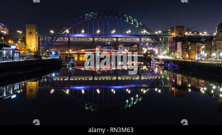 Newcastle, England, Regno Unito - 3 Febbraio 2019: ponti tra Newcastle e Gateshead sono illuminate di notte e si riflette nelle acque del fiume Tyne. Foto Stock