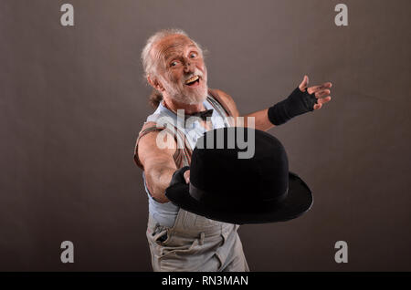 Vecchio allegro hobo che posano con logora, black hat, studio shot contro uno sfondo grigio Foto Stock