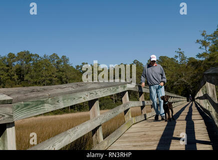 Visita di un maschio caucasico con cane sulla passerella al Vereen Memorial Historical Gardens Little River, South Carolina USA. Foto Stock