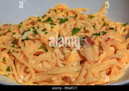 Vista ravvicinata di un piatto di deliziosa preparata di fresco italiano spaghetti alla carbonara con prosciutto, uova e formaggio parmigiano, guarnito con basilico in un piccolo rustico res Foto Stock