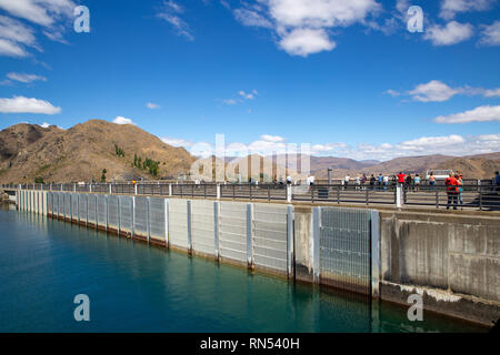 Linea di turisti la strada lungo la diga per scattare foto di Benmore power station e la scena di fiume di gran lunga al di sotto, in Nuova Zelanda Foto Stock