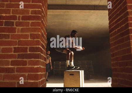 I giovani africani atleta maschio facendo salti plyo allenamento endurance in palestra crossfit. Il salto sulla scatola. Fase touchdown. Foto Stock