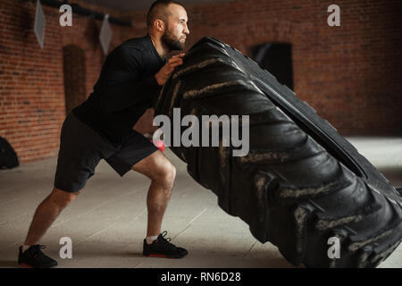 CrossFit tecnica dei pneumatici. Potente bodybuilder dimostra regole e ordine di formazione con improvvisato powerlifting elemento nel fitness club Foto Stock