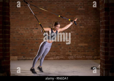 Donna Fitness trainin sul ricetrasmettitore TRX in palestra, fare esercizio in cui i muscoli di stabilizzazione sono addestrati e tutto il corpo è al lavoro, il che rende tale lavoro Foto Stock