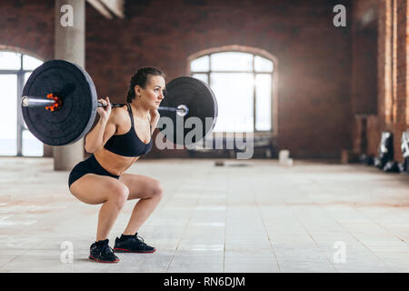 Ben costruito ragazza potente facendo squat con pesanti barbell. vista laterale a piena lunghezza foto.spazio copia Foto Stock