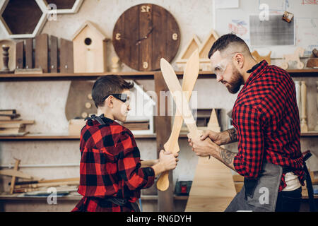 Relazioni familiari, la paternità, hobby, falegnameria, concetto di falegnameria - padre e figlio la riproduzione di cavalieri con legno spade DIY al workshop di falegname Foto Stock