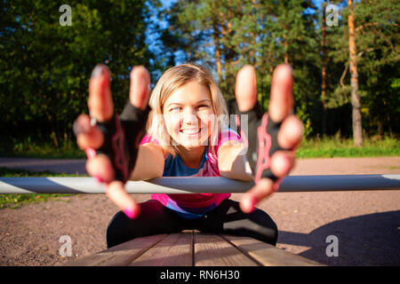 Atleta ragazza tirando le mani avanti esercita a panca in legno in posizione di parcheggio d'estate. Foto Stock