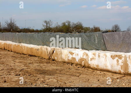 Protezione antiesondazione temporanea di una parete realizzata in due strati di barriere box coperti con il bianco e il grigio panno in geotessile utilizzato per proteggere case famiglia Foto Stock